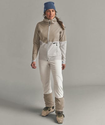 Eine Frau in Skibekleidung mit einer beige Jacke und weißen Hosen.