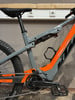 Graues und oranges Mountain-E-Bike mit Dämpfer und Pedalen.