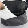 Ein weißer Sportschuh wird in eine dunkelgraue Tasche gesteckt.