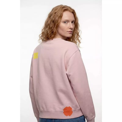 Eine rothaarige Frau trägt einen rosafarbenen Pullover mit gelbem und orangem Aufnäher. Eine rothaarige Frau trägt einen rosafarbenen Pullover mit gelbem und orangem Aufnäher.