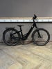 Schwarzes E-Bike mit Gepäckträger und Schutzblechen auf Holzboden.