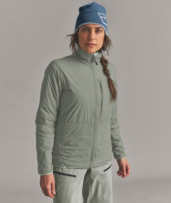 Eine Frau in einer blauen Mütze und einer grünen Jacke steht vor einem grauen Hintergrund. Eine Frau in einer blauen Mütze und einer grünen Jacke steht vor einem grauen Hintergrund.