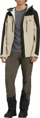 Ein Mann in einer beige Jacke mit dunkelgrünen Ärmeln und brauner Hose. Ein Mann in einer beige Jacke mit dunkelgrünen Ärmeln und brauner Hose.