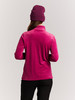 Eine Frau von hinten in einem rosa Pullover mit Zopfmuster und lila Mütze.