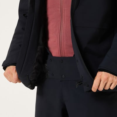 Detail eines Mannes in einer dunklen Jacke und einem rosa Pullover mit offenem Reißverschluss.