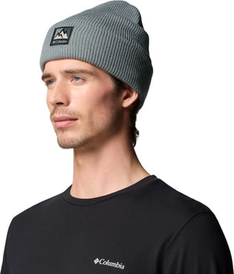 Ein Mann in einer grauen Mütze mit einem Berglogo und einem schwarzen Columbia-T-Shirt. Ein Mann in einer grauen Mütze mit einem Berglogo und einem schwarzen Columbia-T-Shirt.