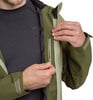 Ein Mann schließt den Reißverschluss einer grünen Jacke über einem dunklen Hemd.