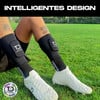 Mann in Schienbeinschonern und weißen Fußballschuhen auf Rasen.