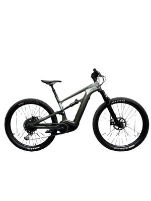 Ein graugrünes vollgefedertes E-Bike mit schwarzen Maxxis-Reifen. Ein graugrünes vollgefedertes E-Bike mit schwarzen Maxxis-Reifen.
