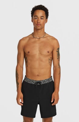 Ein Mann mit Tattoos auf Brust und Armen trägt eine schwarze Badehose.
