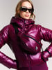 Frau in glänzender weinroter Jacke mit Bauchtasche und Sonnenbrille.