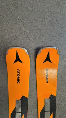 Zwei orange Atomic-Ski mit schwarzem Logo auf grauer Oberfläche.
