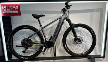 Graues Genesis E-Bike auf einem Ständer mit Beschriftung oben links.