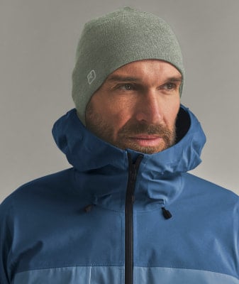 Ein Mann in einer blauen Jacke und einer grauen Mütze mit Logo.
