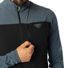 Ein Mann öffnet eine schwarze Jacke mit grauen Ärmeln und Logo.