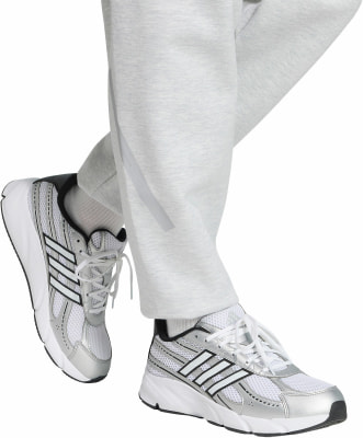 Weiße Adidas-Sneaker mit schwarzen Streifen auf hellgrauer Jogginghose. Weiße Adidas-Sneaker mit schwarzen Streifen auf hellgrauer Jogginghose.