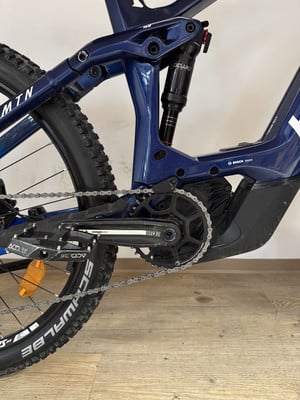Detail des hinteren Teils eines dunkelblauen Mountain-E-Bikes mit Dämpfer und Kette. Detail des hinteren Teils eines dunkelblauen Mountain-E-Bikes mit Dämpfer und Kette.