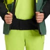 Ein Mann öffnet seine grüne Jacke mit einem schwarzen Streifen am Bauch.