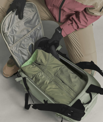 Eine Person packt eine grüne Jacke in einen hellgrünen Rucksack. Eine Person packt eine grüne Jacke in einen hellgrünen Rucksack.