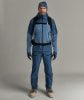 Ein Mann in einer blauen Skijacke, Hose, Mütze und Handschuhen mit Rucksack.