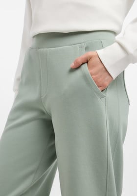 Eine Frau steckt ihre Hand in die Tasche einer hellgrünen Hose mit weißer Bluse.