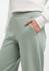 Eine Frau steckt ihre Hand in die Tasche einer hellgrünen Hose mit weißer Bluse.