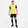 Ein Mann in einem gelben Hemd und schwarzer Hose mit schwarzen Socken und Schuhen.