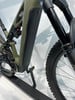 Grünes E-Bike mit schwarzem Akku und Federung auf einem Ständer.