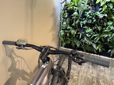 Der Lenker eines E-Bikes mit Display und Griffen vor einer grünen Wand. Der Lenker eines E-Bikes mit Display und Griffen vor einer grünen Wand.