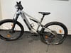 Ein silbernes E-Mountainbike mit Federung und Scheibenbremsen auf dunklem Teppich.