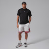 Ein Mann in einem schwarzen T-Shirt und weißen Shorts mit roter Paspel steht.