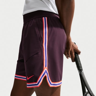 Mann in dunkelvioletten Shorts mit bunten Streifen hält einen Tennisschläger. Mann in dunkelvioletten Shorts mit bunten Streifen hält einen Tennisschläger.