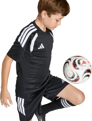Ein Junge im schwarzen Fußballtrikot mit weißen Streifen spielt mit einem Ball.