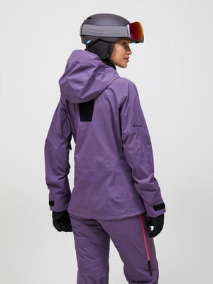 Eine Frau in einer lila Skijacke und Hose, mit Helm und Brille. Eine Frau in einer lila Skijacke und Hose, mit Helm und Brille.