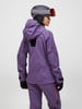 Eine Frau in einer lila Skijacke und Hose, mit Helm und Brille.