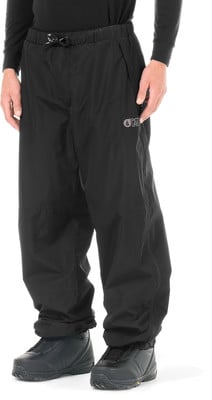 Ein Mann trägt eine schwarze Outdoor-Hose mit Logo und schwarzen Stiefeln.