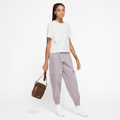 Eine Frau in einem weißen T-Shirt und lila Jogginghose mit brauner Tasche.