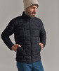 Mann in dunkler Daunenjacke und beigem Hut mit den Händen in den Taschen.