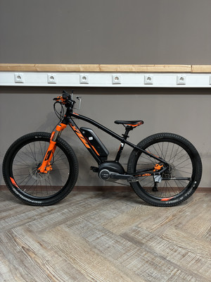 Schwarzes E-Bike mit orangefarbenen Details auf Holzboden.