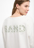Damenpullover mit grüner SAND-Aufschrift auf dem Rücken.
