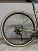 Ein goldenes Fahrrad mit beigen Reifen und schwarzen Felgen vor grauem Hintergrund.