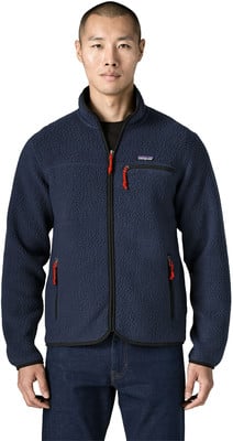 Ein Mann in einer dunkelblauen Fleecejacke mit roten Reißverschlüssen und Jeans.