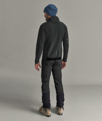 Mann in dunkler Jacke, Hose und blauer Mütze mit Skischuhen.