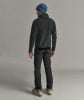 Mann in dunkler Jacke, Hose und blauer Mütze mit Skischuhen.