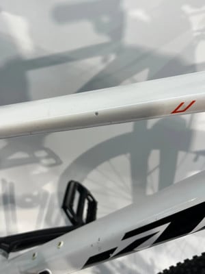 Nahaufnahme eines weißen Fahrradrahmens mit kleinem Punkt und Logo. Nahaufnahme eines weißen Fahrradrahmens mit kleinem Punkt und Logo.