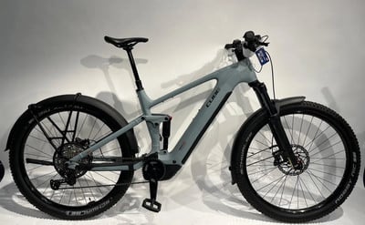 Ein graues Cube E-Bike mit Federung und Schutzblechen steht vor weißem Hintergrund.