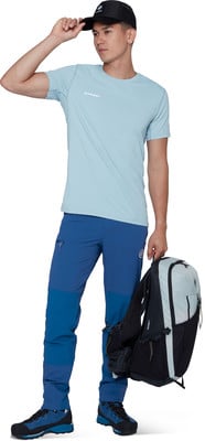 Ein Mann in blauer Hose, hellblauem T-Shirt und schwarzer Kappe hält einen Rucksack. Ein Mann in blauer Hose, hellblauem T-Shirt und schwarzer Kappe hält einen Rucksack.