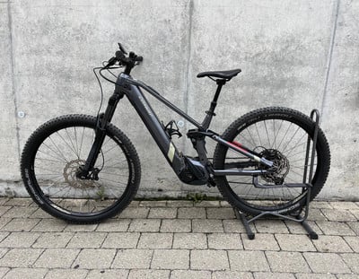 Ein graues E-Bike mit schwarzen Rädern und Federung steht vor einer Wand. Ein graues E-Bike mit schwarzen Rädern und Federung steht vor einer Wand.