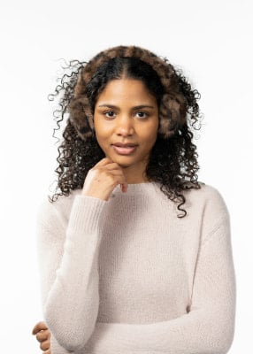 Eine Frau mit lockigem Haar trägt einen beigen Pullover und Fell-Ohrenschützer. Eine Frau mit lockigem Haar trägt einen beigen Pullover und Fell-Ohrenschützer.
