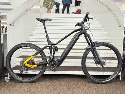 Schwarzes E-Bike mit Federung auf einer Treppe, gelbe Rahmendetails. Schwarzes E-Bike mit Federung auf einer Treppe, gelbe Rahmendetails.